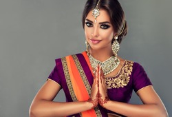 Portrait of a beautiful indian girl in a greetting pose to Namaste hands .India woman in traditional sari dress and jewelry.