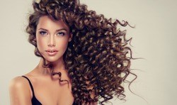 Brunette  girl with long  and   shiny curly  hair .  Beautiful  model woman  with wavy hairstyle