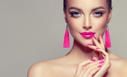Beautiful model girl with pink fuchsia manicure on nails . Fashion makeup and cosmetics . Large earrings tassels jewelry Magenta color .