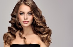 Brunette  girl with long  and   shiny curly hair .  Beautiful  model woman  with curly hairstyle   .Care and beauty of hair