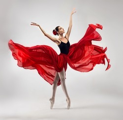 Ballerina. Young graceful woman ballet dancer, dressed in professional outfit, shoes and red weightless skirt is demonstrating dancing skill. Beauty of classic ballet.