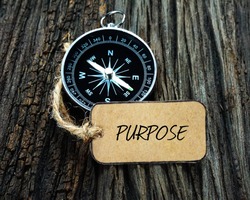 PURPOSE inscription written on paper tag, compass on old wooden background.
