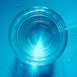 Top view of fresh water in a glass with water drops on blue background.