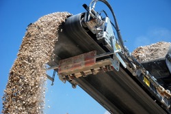 aggregate production by mobile crusher. Conveyor belt of a working mobile crusher machine, close-up, with blown away by the wind white stone dust against a blue sky.