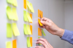 IT worker tracking his tasks on kanban board. Using task control of agile development methodology. Man attaching sticky note to scrum task board in the office