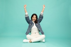 Attractive beautiful Asian woman sitting on floor and hands up raised arms from happiness isolated on green background, Excited businesswoman winner success concept