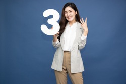 Young beautiful Asian woman showing number 3 and pointing up with finger number three isolated on blue background