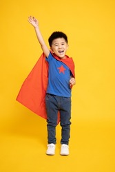 Smiling Superhero Asian boy in red cape isolated yellow background, Full body composition