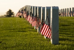 Endless row of white marble gravestones continues above hilltop at the Fort Logan National Cemetery in Denver, Colorado. American flags decorating each grave to mark the Memorial Day.