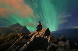 Women tourists sit at the top of the rock with Northern Lights or Aurora Borealis, Beautiful landscape.