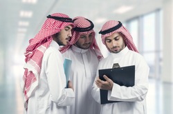 Arab business people in a meeting, three business people standing in a modern office interior discussing work, ethnic business people, business team.