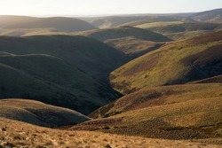 Distant views of Hindside Knowe center top from the ridge leading to Windy Gyle in the Cheviot mountains at sunrise in Northumberland.