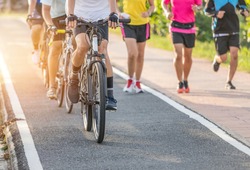Close up movement group of cyclists during ride bicycle with male runner jogging for exercise on the road park in sunset time healthy lifestyle concept 