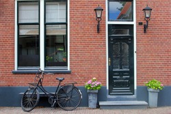Facade of typical Dutch house with brick walls, steps, front door windows and black bike in popular neighborhood street, Netherlands