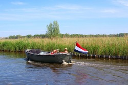 Couple is sailing at river in motor sloop boat with waving Dutch flag, Loosdrechtse Plassen, Loosdrecht, Netherlands 