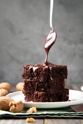 Chocolate spongy brownie cakes with walnuts and a spoon pouring melted chocolate topping 