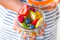 Little girl hands showing a fruit salad on a jar. Healthy snack for children concept
