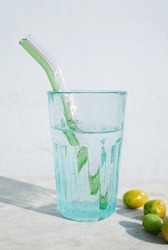Beautiful blue drinking glass made of bubble glass full of water with 2 colorful glass straws. Still life of a teal transparent cup and small tomatoes as a snack