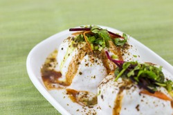 Closeup of Dahi Vadas (a popular snack famous all over India prepared by soaking lentil dumplings or vadas in thick dahi or yogurt) dunked in a creamy whipped yogurt topped with spicy & sweet chutney