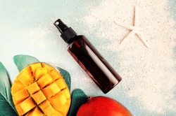 Cosmetic product in spray bottle top view summer skin care background, mango fruit, beach sand, pastel toned. Summertime beauty treatment, safe, natural, and aromatic