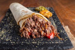 Tortilla with pulled beef meat, onion and tomato serving on black plate with humus and jalapeno pepper.