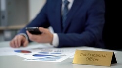 Chief financial officer checking data in annual report, using smartphone, work