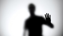 Shadow of man holding glass wall, trying to escape from captivity, kidnapping
