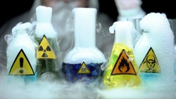 Marked dangerous liquids evaporating in flasks in front laboratory worker