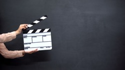 Female hands using clapperboard against black background, shooting movies