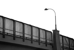 Black and white, monochrome silhouette image of a wrought iron decorative street lamp on a bridge against the backdrop of bright, clear, white, featureless, blank summer sky. Copy space.