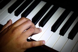 Close-up of a young performer's hand playing the piano with vignetting to focus attention on the main sibject.