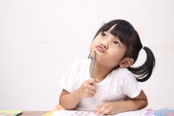 Cute litle Asian baby girl holding pen and book, studying and learning while thinking something or having good idea, smiling and looking up, imagination with copy space