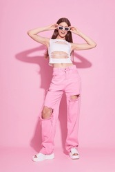 Young fashion woman in pink trendy jeans and white top on pink background. Platform slides sandals, y2k, monochrome, violet bright  makeup.