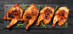 Halves of appetizing grilled juicy chicken with golden brown crust served with lemon slices,barbeque  sauce and rosemary.