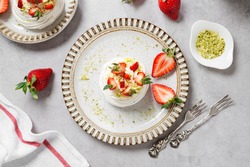 Perfect mini Pavlova cake with whipped mascarpone cream and fresh strawberry slices, sprinkled with crushed pistachios. top view
