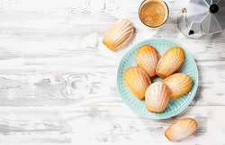 Perfect French madeleine cookies, buttery and delicate, powdered with icing sugar served with cup of coffee.  White wooden  background. Top view