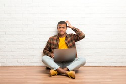 African american man sitting on the floor with his laptop with an expression of frustration and not understanding