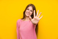 Young woman with long hair over isolated yellow wall counting five with fingers
