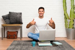 Handsome man sitting on the floor with his laptop giving a thumbs up gesture