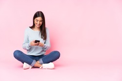 Young caucasian woman isolated on pink background sending a message with the mobile