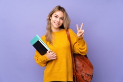 Teenager Russian student girl isolated on purple background showing victory sign with both hands
