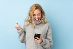 Young blonde woman wearing a sweater isolated on blue background surprised and sending a message