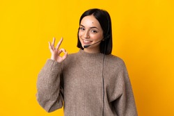 Young telemarketer woman isolated on yellow background showing ok sign with fingers