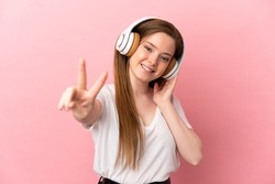 Teenager girl over isolated pink background listening music and singing