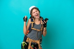 Young English rock climber woman isolated on blue background with phone in victory position