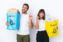 Young couple holding a bag full of plastic and paper to recycle isolated on white background showing and lifting a finger in sign of the best