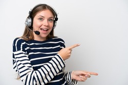 Telemarketer caucasian woman working with a headset isolated on white background surprised and pointing side