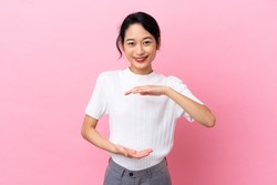 Young Vietnamese woman isolated on pink background holding copyspace imaginary on the palm to insert an ad
