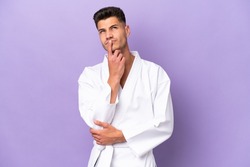 Young caucasian man doing karate isolated on purple background having doubts while looking up