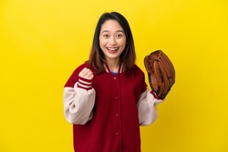Young Vietnamese player woman with baseball glove isolated on yellow background celebrating a victory in winner position